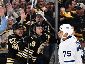 Bruins’ John Beecher celebrates with Hamphus Lindholm after scoring a goal as Maple Leafs’ Ryan Reaves skates by in Boston on Saturday night.