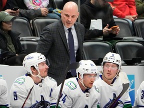 Vancouver Canucks head coach Rick Tocchet, back, confers with center J.T. Miller, front left, center Pius Suter and right wing Brock Boeser, front right, in the second period of an NHL hockey game against the Colorado Avalanche Tuesday, Feb. 20, 2024, in Denver.