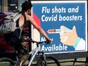 A cyclist makes their way past a pharmacy advertising flu and COVID booster shots, in Edmonton Thursday, Aug. 15, 2024.