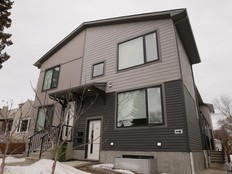 A grey house with two front doors sits against a overcast sky.