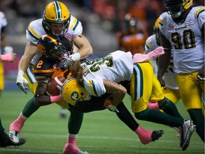 Edmonton Eskimos defensive back Aaron Grymes and linebacker Adam Konar, left, tackle B.C. Lions ball carrier Chris Rainey in Vancouver, B.C., on Oct. 21, 2017.