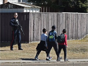 School children walk past a police officer as the tactical unit surround a complex on 82 Street near 144 Avenue on Monday.