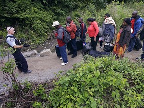 A Royal Canadian Mounted Police officer, left, standing in Saint-Bernard-de-Lacolle, Quebec, advises migrants that they are about to illegally cross from Champlain, N.Y., and will be arrested, Monday, Aug. 7, 2017. (AP Photo/Charles Krupa)