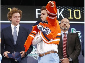 Evan Bouchard, middle, puts on a jersey after being selected by the Edmonton Oilers during the NHL hockey draft in Dallas, Friday, June 22, 2018.