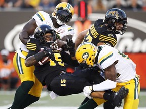 Hamilton Tiger-Cats' Alex Green gets tackled by Edmonton Eskimos Almondo Sewell, left, and Alex Bazzie, right, during the first half of CFL football action in Hamilton on Aug. 23, 2018.
