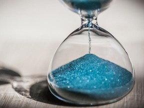 Sand running through the bulbs of an hourglass measuring the passing time in a countdown to a deadline, on a bright wooden background with copy space.