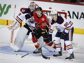 Edmonton Oilers goalie Mikko Koskinen, left, and teammate Logan Day, sandwich Calgary Flames' Andrew Mangiapane during preseason NHL action in Calgary on Sept. 17, 2018.