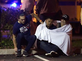 People comfort each other as they sit near the scene Thursday, Nov. 8, 2018, in Thousand Oaks, Calif., where a gunman opened fire Wednesday inside a country dance bar crowded with hundreds of people on college night.