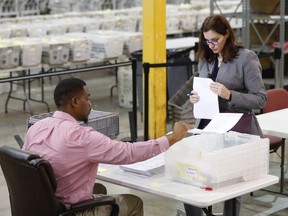 A Republican party observer, right, watches as an employee at the Palm Beach County Supervisor Of Elections office goes through a stack of damaged ballots, Thursday, Nov. 15, 2018, in West Palm Beach, Fla.