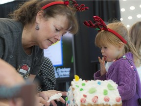 Debbie Mears is helped with the icing on the Adopt-A-Teen gingerbread house by three-year-old Lidia Lee. The Christmas Bureau launched its 78th campaign with a gingerbread house decorating challenge in Ford Hall at Rogers Place.