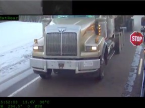 A screenshot from a school bus video captured by the High Prairie school division as a semi-truck fails to stop for a school bus with its red lights flashing and stop signs extended. The board chair said vehicle "flybys" are a frequent problem that put children at risk.