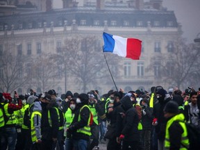 Demonstrators gather near the Arc de Triomphe as a French flag floats during a protest of Yellow vests (Gilets jaunes) against rising oil prices and living costs, on December 1, 2018 in Paris. - Anti-government protesters torched dozens of cars and set fire to storefronts during daylong clashes with riot police across central Paris on December 1, as thousands took part in fresh "yellow vest" protests against high fuel taxes.