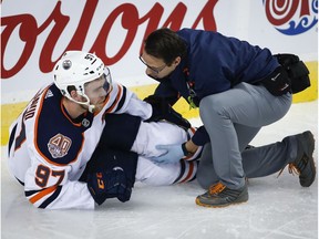 Edmonton Oilers' Connor McDavid, left, has his knee tended too after crashing into Calgary Flames goalie Mike Smith during second period NHL hockey action in Calgary, Saturday, April 6, 2019. McDavid left his team's season finale with a left leg injury after a hard collision with the net against the Calgary Flames on Saturday.