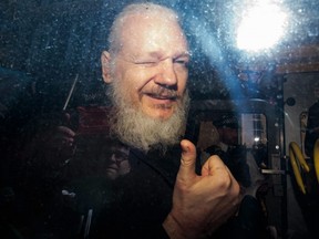 Julian Assange gestures to the media from a police vehicle on his arrival at Westminster Magistrates court on Thursday, April 11, 2019 in London, England.