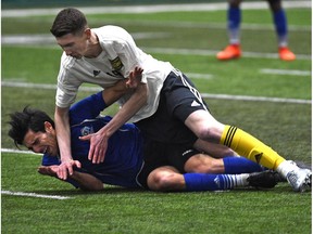 University of Alberta Golden Bears Easton Ongaro (19) falls on FC Edmonton Mauro Eustaquio (blue) during an exhibition game between the two teams at Foote Field in Edmonton, Tuesday, March 7, 2017.