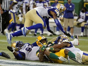 Winnipeg Blue Bombers Chandler Fenner leaps over Edmonton Eskimos Ricky Collins Jr. (middle) after he is tackled by Bombers Drake Nevis (left) and Marcus Rios (right) during Canadian Football League game action in Edmonton on Friday August 23, 2019.