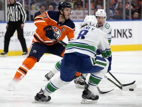 The Edmonton Oilers captain Connor McDavid (97) battles the Vancouver Canucks' Christopher Tanev (8) and Tim Schaller (59) during third period NHL action, in Edmonton Saturday Nov. 30, 2019.
