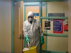A worker in protective clothing, including face mask and gloves, carries a bucket as he works inside of The County Oak Medical Centre in Brighton, southern England on February 10, 2020, after it closed for "urgent operational health and safety reasons," following reports a member of staff was infected with the 2019-nCoV strain of the novel coronavirus.