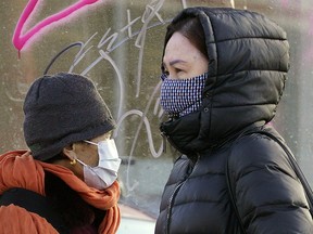 Two pedestrians, wearing face masks for protection against COVID-19 in downtown Edmonton on March 17, 2020.