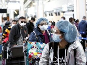 People wearing face masks and goggles wait to check in for an international flight at the Vancouver International Airport after Canada's Prime Minister Justin Trudeau announced additional measures to combat the spread of the coronavirus disease (COVID-19), in Richmond, B.C., Monday, March 16, 2020.