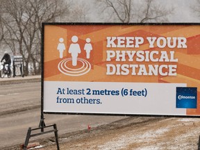 People pass near a City of Edmonton sign calling for physical distancing during the COVID-19 coronavirus pandemic along River Valley Road in Edmonton, on Monday, March 30, 2020. Physically distancing by a minimum of two metres or six feet is required during the COVID-19 pandemic to prevent the spread of the novel coronavirus.