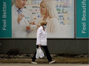 A woman walks past a sign outside a pharmacy in downtown Edmonton during the COVID-19 pandemic on April 30, 2020.