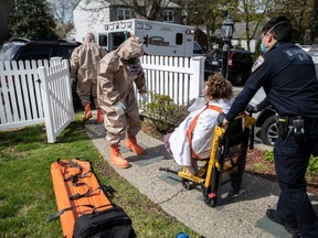 Yonkers Fire Department EMTs, clothed in full personal protective equipment, assist an Empress EMS medic to transport a patient with COVID-19 symptoms to a hospital on April 14, 2020 in Yonkers, N.Y.