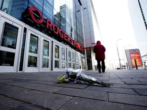 A pedestrians walks past a bouquet of flowers left outside Rogers Place Saturday morning following the death of Edmonton Oilers forward Colby Cave, April 11, 2020.