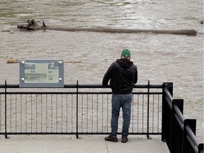 A pedestrian watches debris float down the North Saskatchewan River from Louise McKinney Riverfront Park, in Edmonton Saturday May 23, 2020. On Friday the City warned residents to stay away from the rapidly-rising water of the North Saskatchewan River.
