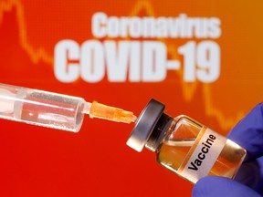 A small bottle labeled with a "Vaccine" sticker is held near a medical syringe in front of displayed "Coronavirus COVID-19" words in this illustration taken April 10, 2020.