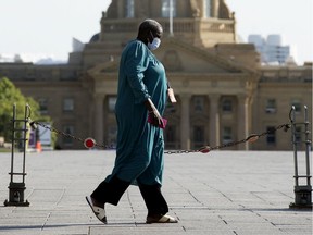 A pedestrian wears a face mask while walking past the Alberta Legislature, Aug. 19, 2020.