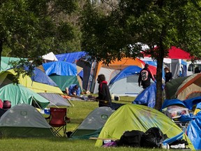 Tents crowd a grassy area in an open field, with people seen walking about.