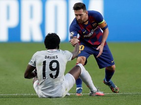 Barcelona's Lionel Messi helps Bayern Munich's Alphonso Davies back up, as in Champions League play at the Benfica Stadium in Lisbon, Portugal on Aug. 14, 2020.
