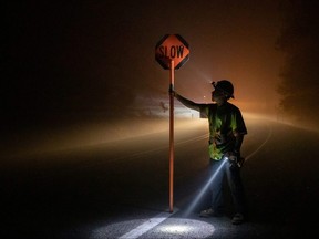 Bryan Alvarez holds a sign for oncoming traffic as utility workers repair power lines in the aftermath of the Obenchain Fire in Eagle Point, Ore., Friday, Sept. 11, 2020.
