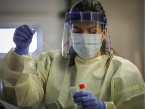 An Alberta Health Services worker holds a COVID-19 swab at a drive-thru assessment centre.