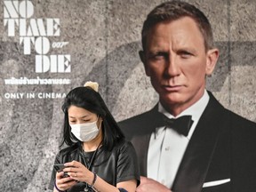 In this file photo taken on February 27, 2020 a woman wearing a facemask amid fears of the spread of the COVID-19 novel coronavirus walks past a poster for the new James Bond movie "No Time to Die" in Bangkok.