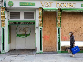 A woman wearing a protective face covering as a precaution against the spread of COVID-19 walks past a boarded up bar in Dublin on October 21, 2020.