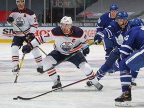 Connor McDavid #97 of the Edmonton Oilers tries to grab a loose puck from T.J. Brodie #78 and Ilya Mikheyev #65 of the Toronto Maple Leafs during an NHL game at Scotiabank Arena on January 20, 2021 in Toronto, Ontario, Canada. The Oilers defeated the Maple Leafs 3-1.