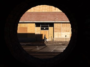 A woman walks past a boarded up former car dealership at 106 Street and 103 Avenue in Edmonton, on Friday, Jan. 15, 2021. The dealership was damaged in a fire. Photo by Ian Kucerak