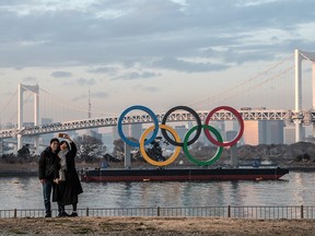 A couple wearing masks takes a selfie in front of the Olympic Rings on January 22, 2021 in Tokyo.