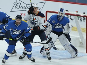 Winnipeg Jets defenceman Derek Forbort (left) deals with Edmonton Oilers forward Jesse Puljujarvi in front of goaltender Laurent Brossoit in Winnipeg on Sun., Jan. 24, 2021.