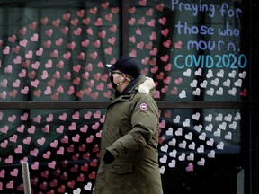 A pedestrian wearing a mask to protect against COVID-19 walks past hundreds of paper hearts posted on the windows of All Saints' Anglican Cathedral, 10035 103 St., in memory of people lost to COVID-19, in Edmonton Thursday Jan. 21, 2021. The paper hearts stretch around the front of the building. Photo by David Bloom