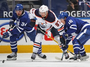 Connor McDavid (97) of the Edmonton Oilers battles for the puck between Auston Matthews (34) and Mitchell Marner (16) of the Toronto Maple Leafs during an NHL game at Scotiabank Arena on March 29, 2021 in Toronto.