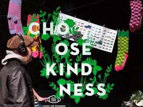 People in COVID-19 masks pass a positve spring sign reading "choose kindness" in the window of John Fluevog Shoes on Whyte Avenue in Edmonton on March 16, 2021.