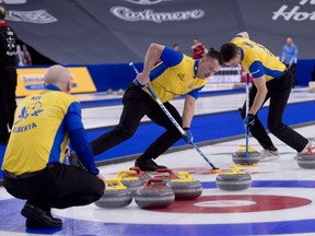 Team Wild Card 2 skip Kevin Koe sits in the rings as Ben Hebert, centre, and John Morris bring the stone into the house against Saskatchwan at the Brier in Calgary, Wednesday, March 10, 2021.