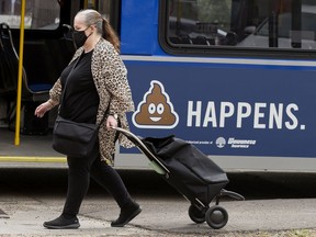 A pedestrian wearing a COVID-19 protective mask makes their way past an advertisement on an ETS bus, along MacDonald Drive near 101 Street, in Edmonton, Thursday May 27, 2021.