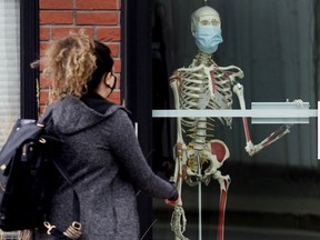 A pedestrian makes their way past a masked skeleton at The PHYSi~YOGIs Ltd, 7525 99 St., in Edmonton Tuesday May 4, 2021. Photo by David Bloom