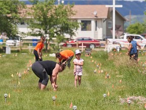 Members of the community place solar lights next to the flags which mark the spots where remains were discovered by ground penetrating radar at the site of the former Marieval Indian Residential School on the Cowessess First Nation in Saskatchewan, Canada, on June 26, 2021. - More than 750 unmarked graves have been found near a former Catholic boarding school for indigenous children in western Canada, a tribal leader said Thursday -- the second such shock discovery in less than a month. (Photo by Geoff Robins / AFP)