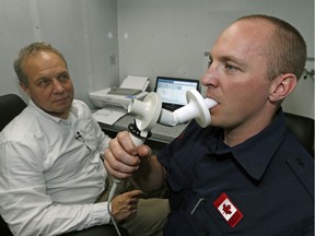 Strathcona County firefighter Jason Biggeman (right) blows into a spirometer to test his lung function in Sherwood Park, Alta. on May 18, 2016. Biggeman was sent to Fort McMurray to fight the Horse River Wildfire. Professor Jeremy Beach of the University of Alberta (left) was part of a team studying the firefighters.
