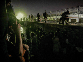 British and Canadian soldiers stand guard near a canal as Afghans wait outside the foreign military-controlled part of the airport in Kabul, hoping to flee the country, on August 22, 2021.